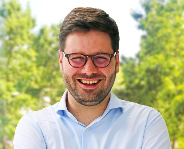 Color portrait of Andrew Owens, smiling at camera. He is wearing a blue shirt and glasses