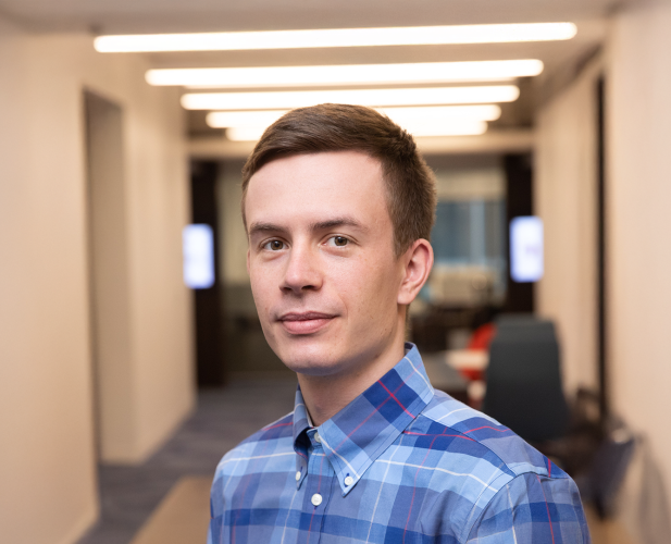 A color photo of a man smiling for a photo in a hallway.