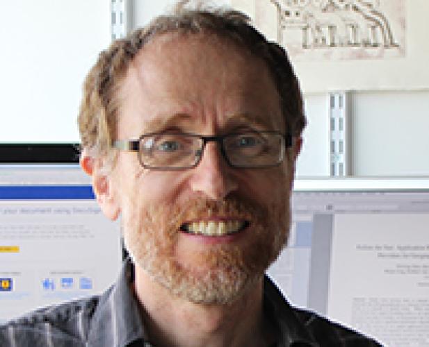 The head and shoulders of a man with glasses, reddish hair and beard, and a striped shirt.