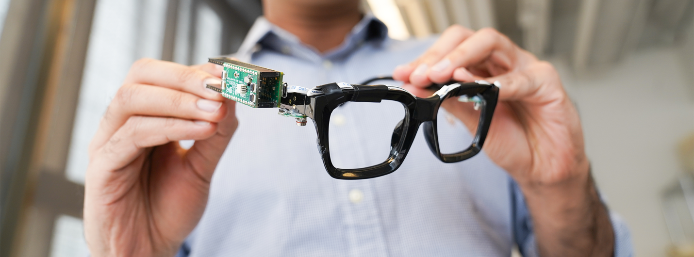 Person holding smart glasses with attached circuit board sensor.