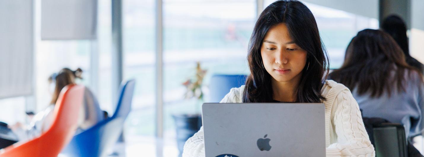 a young female students works on her laptop sitting at a table