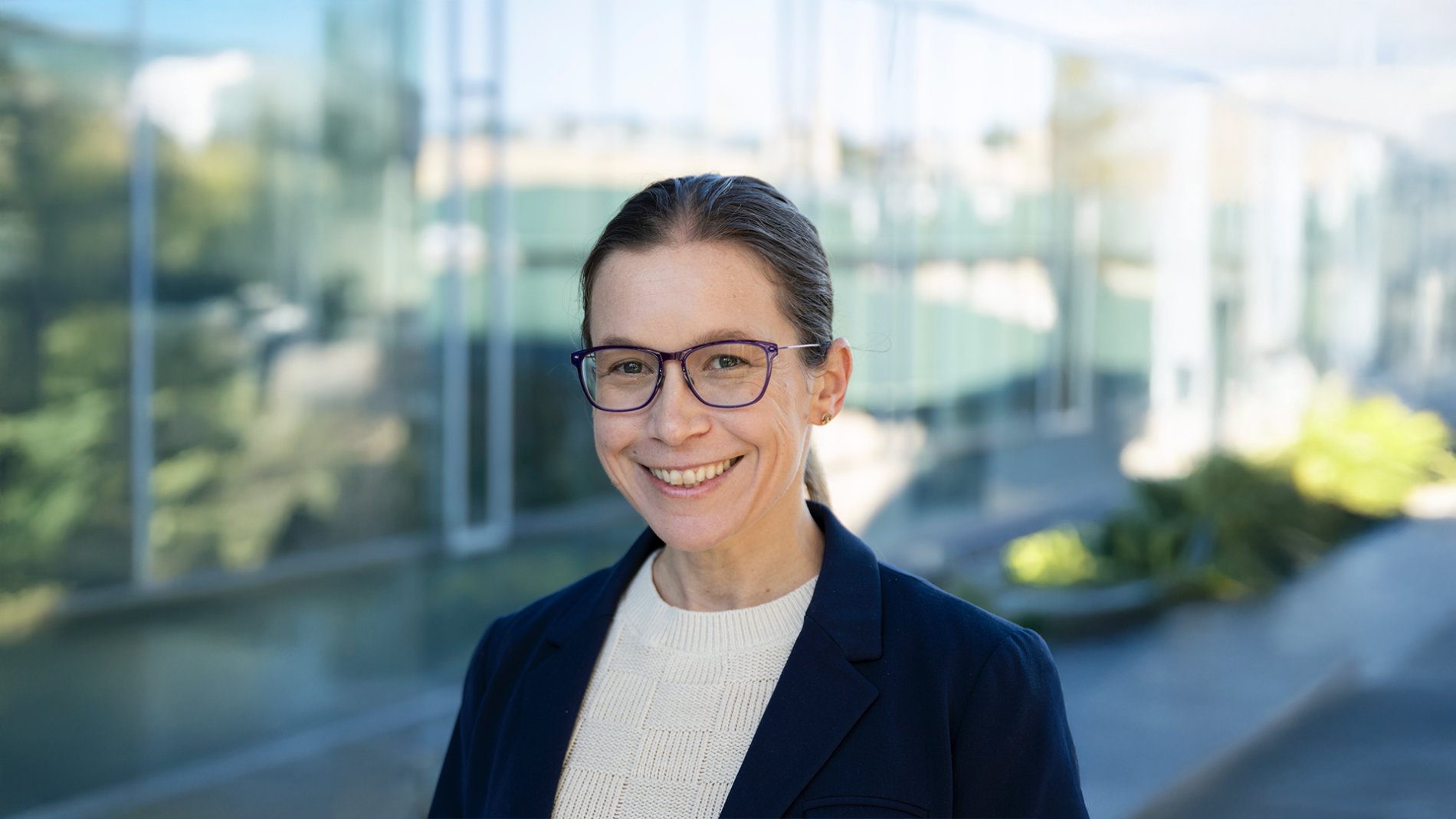 A color photo of a woman standing outside, smiling for a portrait.