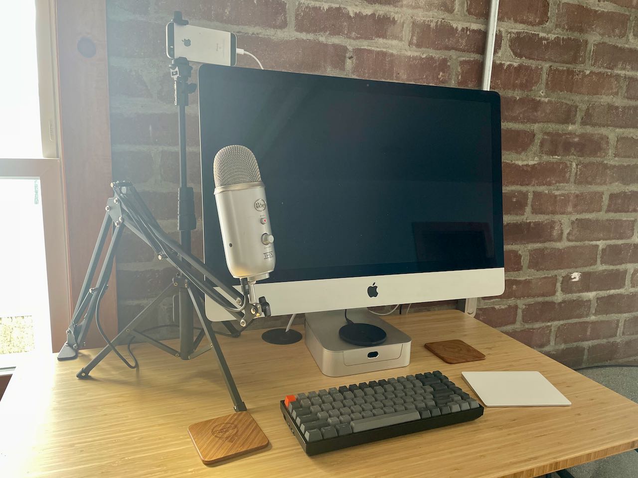 horribly backlit photo of my desk showing the microphone stand and tripod