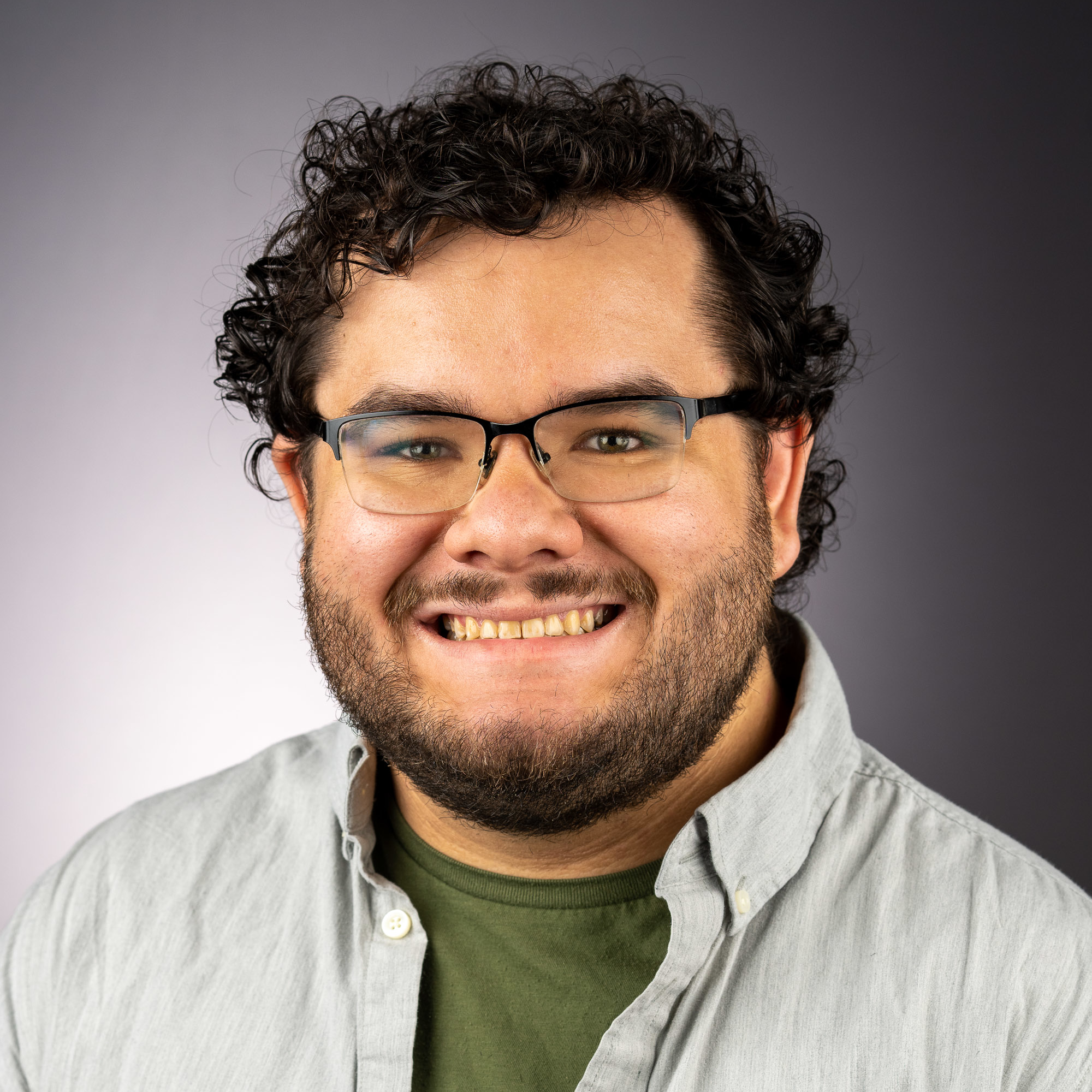 Headshot of Zachary, a smiling man with glasses, curly black hair, and a beard.